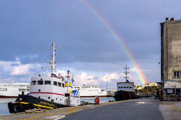 Heraklion, Crete Island / Greece - February 16, 2015: View of a Rainbow over the port of Heraklion city after a rainy morning. Ferry boats and tugboats are docked at the port. Cloudy sky