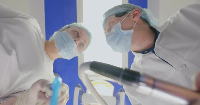 Dental operation. Two doctors treat sick tooth using drilling machine and saliva ejector. Patient POV