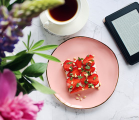breakfast toast with strawberries on a pink plate, black tea in a cup, a bouquet of flowers reader on a marble table