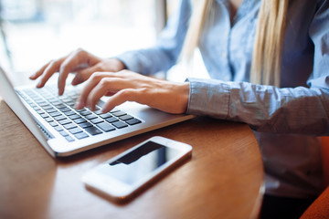 Young woman working in a cafe, keyboard on a laptop computer. Blond student working for netbook after lectures at the university.