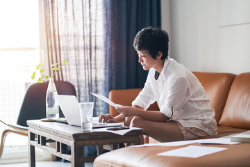 Asian businesswoman sitting on couch  & working on laptop at home