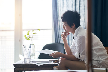 Asian self employed woman sitting on couch  & working on laptop at home