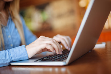 Young woman working in a cafe, keyboard on a laptop computer. Blond student working for netbook after lectures at the university.
