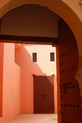 View through arabian style arch into bright sunny empty front court alley in red-orange light with old wooden door - Essaouira, Morocco © Ralf