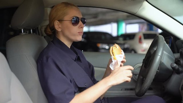 Hungry Woman Cop Eating Burger Sitting In Police Car In Parking Lot, Junk Food