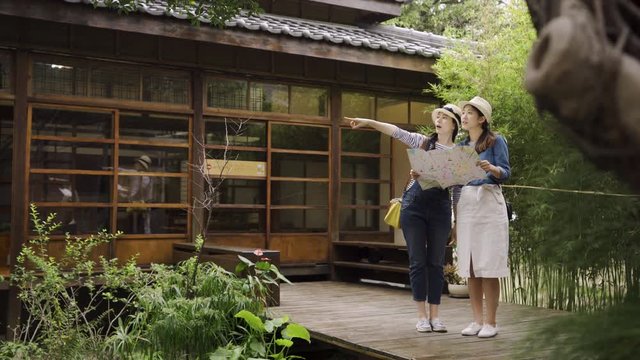two attractive woman travelling to foreign city kyoto japan. girl friends standing near historical monument wooden japanese house. female holding tourist map discussing pointing showing route.