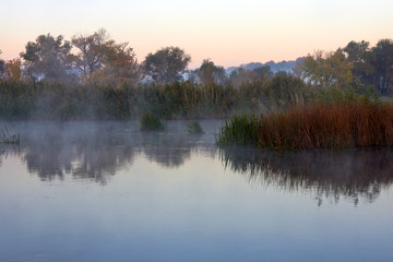 Fototapeta na wymiar Haze over the river in the early autumn morning. Reeds mist fog and water surface on the river at sunrise