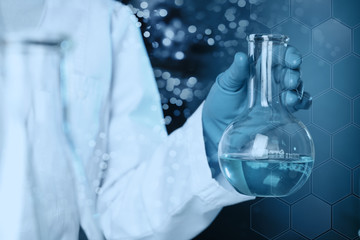Scientist holding glass flask with liquid on color background, closeup. Solution chemistry