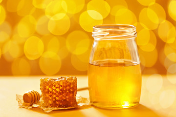 Jar with honey and fresh comb on table against blurred background