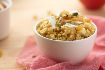 Cooked bulgur with raisins, seeds and coconut in a white bowl on a wooden table. Sweet bulgur porridge, vegetarian food.