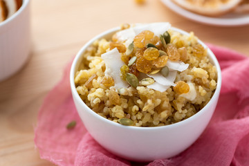 Cooked bulgur with raisins, seeds and coconut in a white bowl on a wooden table. Sweet bulgur porridge, vegetarian food.
