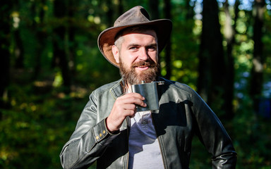 Country style. Bearded man in cowboy hat walk in park outdoor. man hipster relax in autumn forest. Spring weather. camping and hiking. mature male with brutal look drink alcohol from metallic flask
