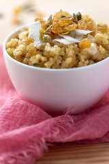 Cooked bulgur with raisins, seeds and coconut in a white bowl on a wooden table. Sweet bulgur porridge, vegetarian food.