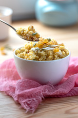 Cooked bulgur with raisins, seeds and coconut in a white bowl and spoon. Sweet bulgur porridge close up, Turkish cuisine.