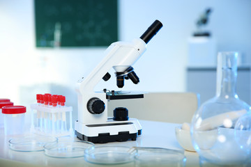 Professional microscope and glassware on table in chemistry laboratory