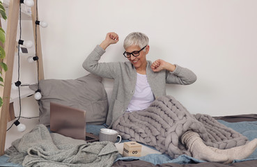 Woman covered with soft woolen blanket, relaxing at home,drinking cacao, using laptop. Cozy and comfy lifestyle