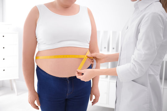 Doctor measuring waist of overweight woman in clinic, closeup