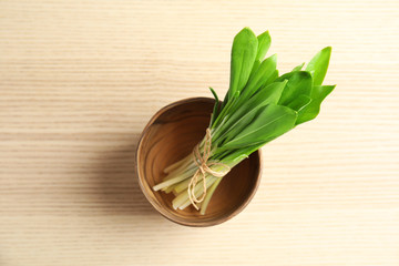 Bowl with bunch of wild garlic or ramson on wooden table, top view
