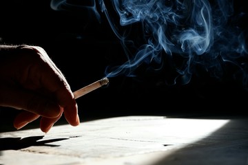 Sunlight and shadow on surface of man's hand holding cigarette with smoke on black background...