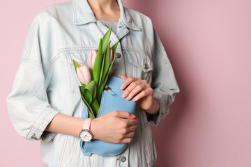 Stylish woman with bag and spring flowers against color background, closeup