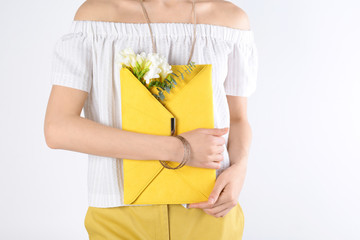 Stylish woman with clutch and spring flowers against light background, closeup