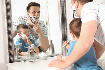 Dad shaving and little son imitating him in bathroom