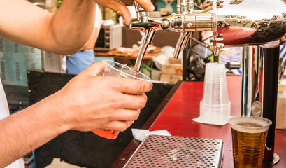 The male bartender pouring beer into a glass close-up. Street food.