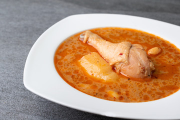 Massaman curry with chicken drumstick or leg and potato in white dish on table.