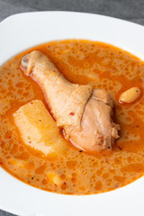 Massaman curry with chicken drumstick or leg and potato in white dish on table.
