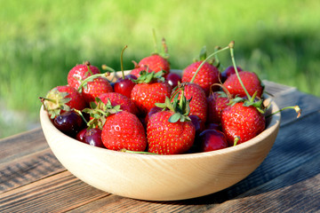 Strawberries and cherries in a wooden bowl on a natural background. Fresh organic summer berries