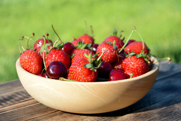 Strawberries and cherries in a wooden bowl on a natural background. Fresh organic summer berries