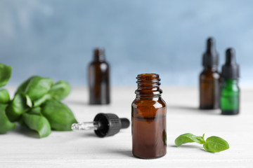 Glass bottle of essential oil, dropper and basil on table