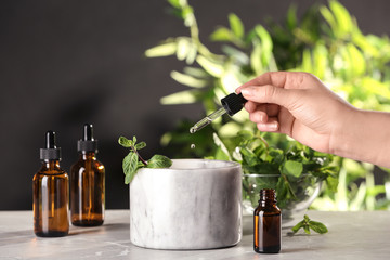 Woman dripping essential oil into mortar with mint on table, closeup