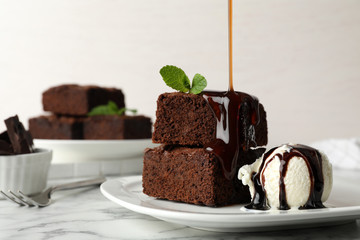 Pouring sauce onto fresh brownies served with ice-cream on plate, space for text. Delicious...