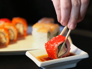 Eating sushi roll set on black background, soy sauce, close-up. Traditional Japanese oriental kitchen