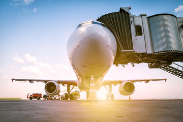 A white passenger airplane stands at the boarding bridge and is loaded with baggage in the rays of...