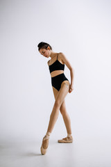 Fashion ballet. Young female ballet dancer in black bodysuit against white studio background. Caucasian ballerina like a fashion model. Style, contemporary choreography concept. Creative art photo.
