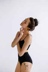 Fototapeta premium Fashion ballet. Young female ballet dancer in black bodysuit against white studio background. Caucasian ballerina like a fashion model. Style, contemporary choreography concept. Creative art photo.