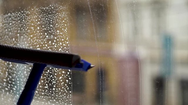 Cleaning windows vertically with a window sweeper squeegee and gloves close up
