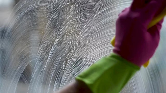Soaping and washing windows with a yellow rug and gloves close up