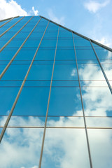 Fragment of a stylish modern high-rise building  with a glazed facade which reflects the blue sky and clouds