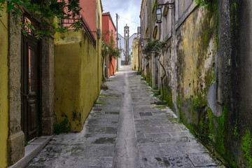 Fototapeta na wymiar Archanes, Crete Island / Greece - March 20, 2019: Narrow paved alley, in Archanes village that leads to a church, with old traditional houses with moss on their walls