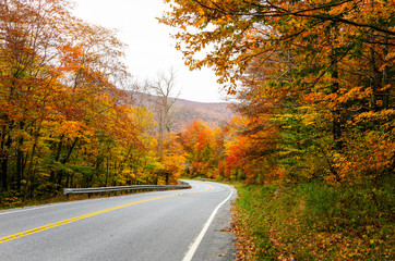 Empty scenic mountain road through a colourful maple tree forest in autumn. Vermont, USA.