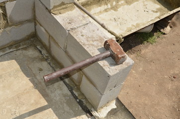  The iron hammer lies on the cinder block on the background of the pan for mixing mortar.