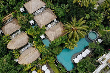 Aerial view of luxury hotel with straw roof villas and pools in tropical jungle and palm trees....