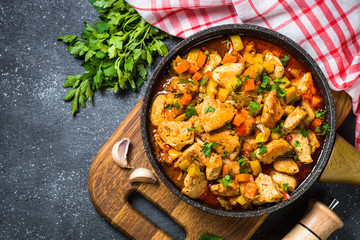 Chicken stew with vegetables black stone table, top view.