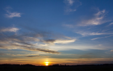 The sun is above the horizon. Sunset over the field, bright clouds in the sky. 