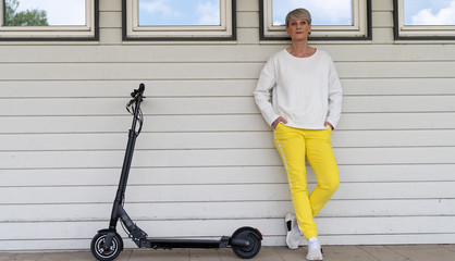 Frau steht lässig an Hauswand mit E-Scooter 
