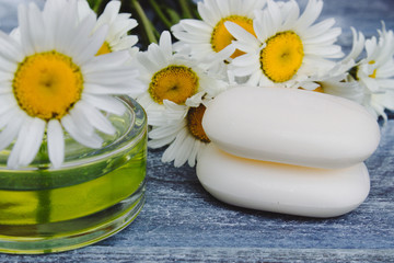 Fototapeta na wymiar Chamomile essential oil in a glass jar next to chamomiles and cosmetic soap.