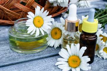Obraz na płótnie Canvas Chamomile essential oil in a glass jar and a bottle near chamomile.